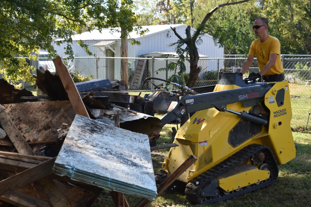 Demolition worker operating a compact track loader to remove wood, concrete, and construction debris from a demolition site.