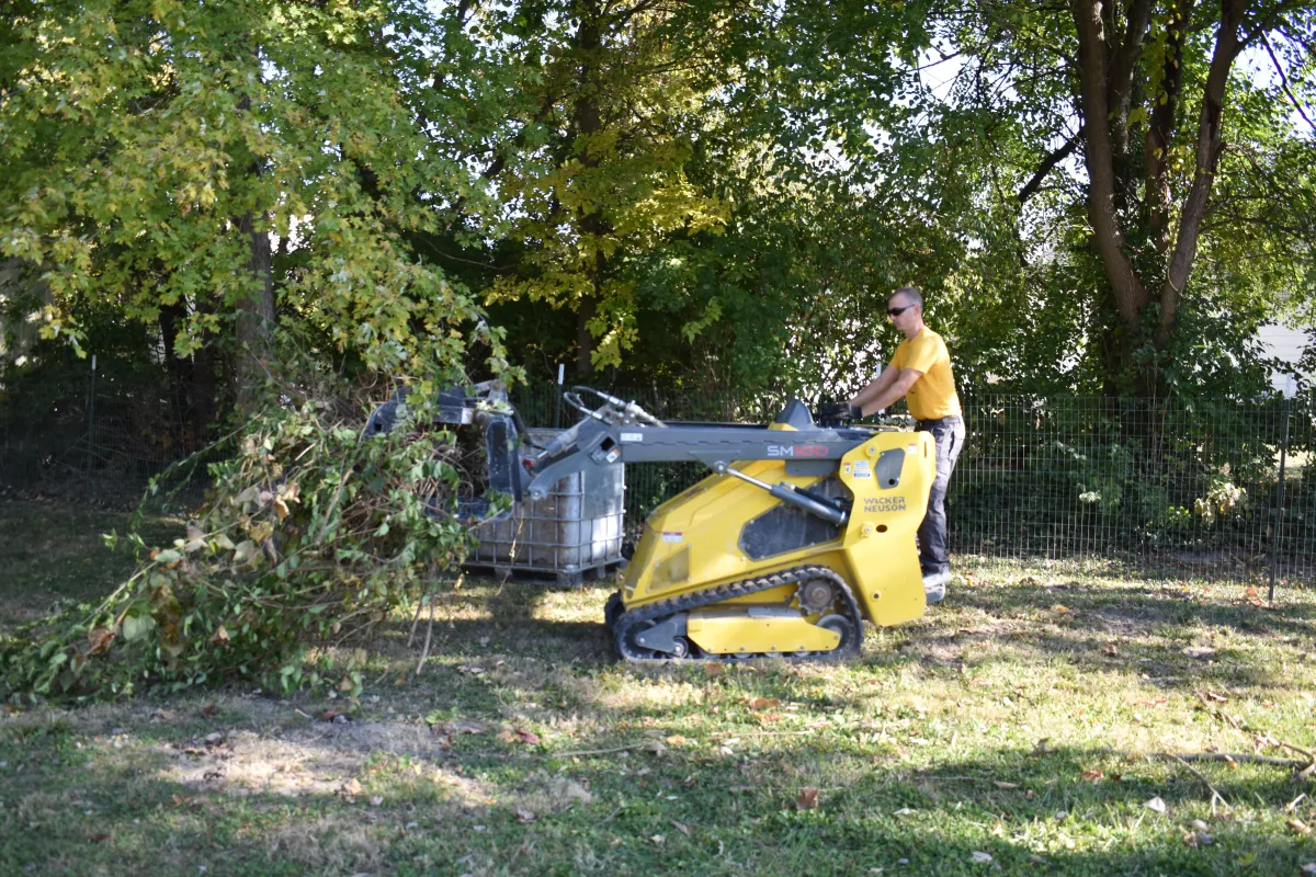 Demolition worker operating a compact track loader to remove wood, concrete, and construction debris from a demolition site.