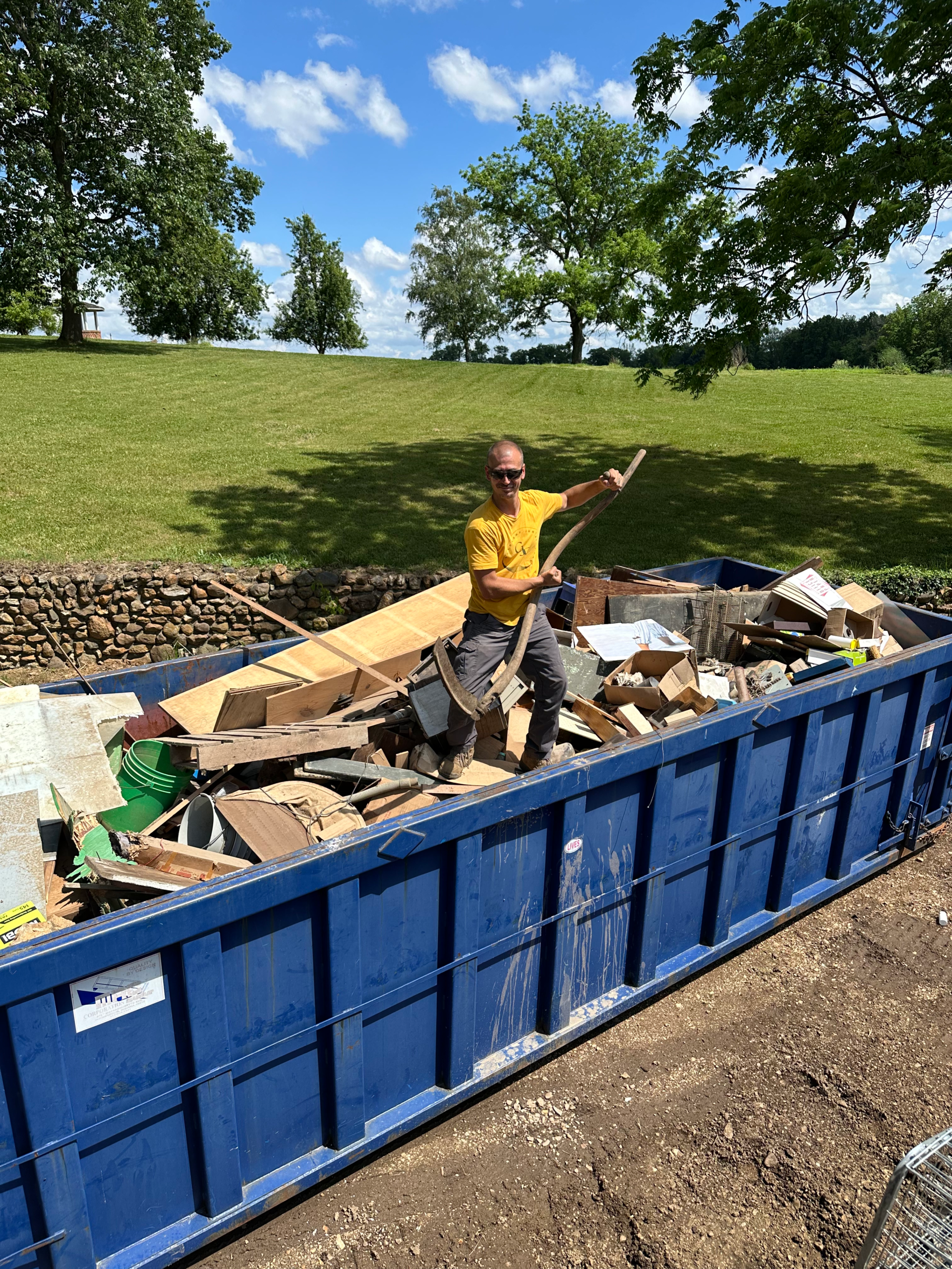 Professional worker efficiently clearing construction and yard debris from a large dumpster as part of a comprehensive yard waste removal service.