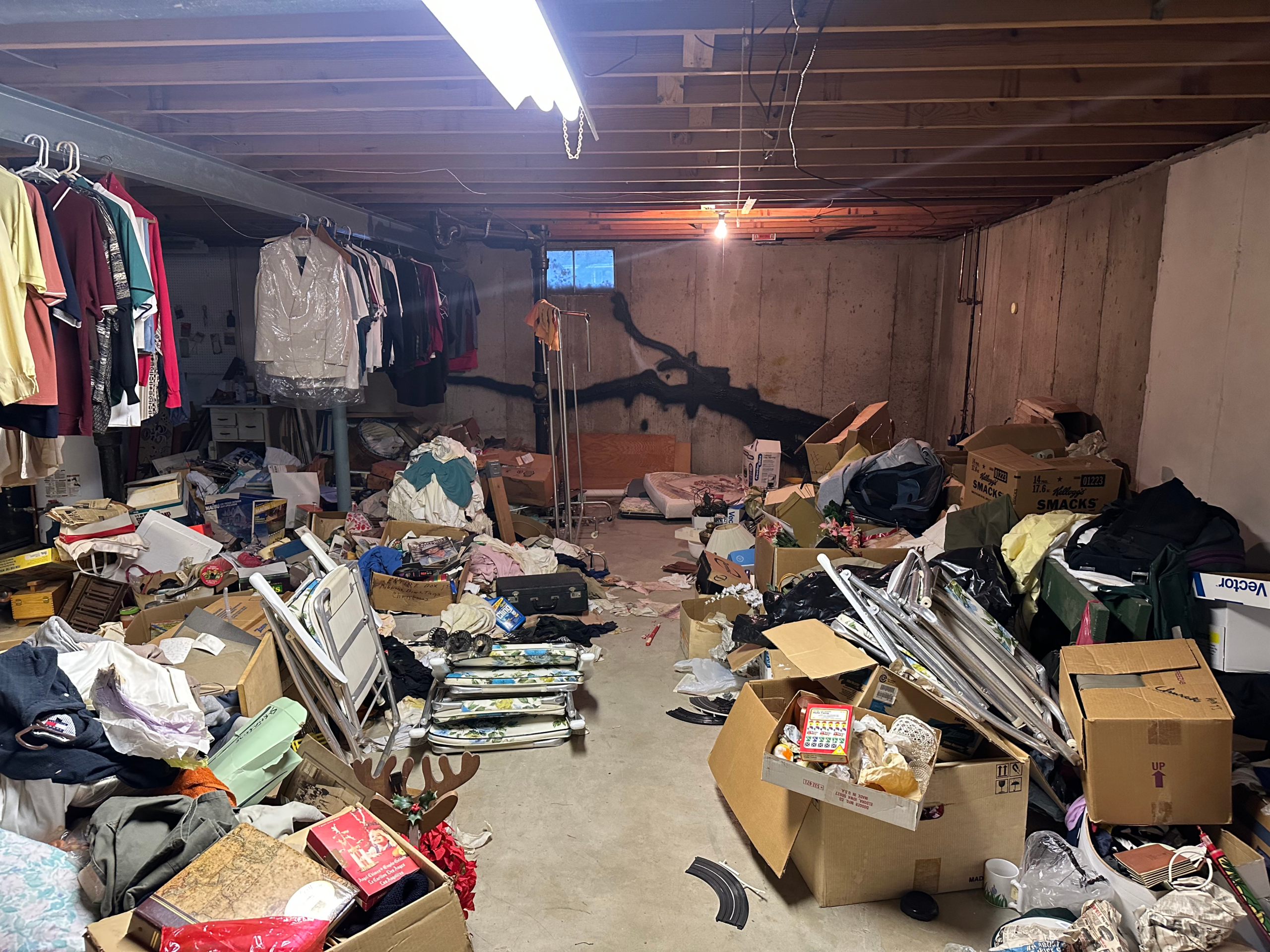 Cluttered, messy basement filled with boxes, old clothes, and junk, needing a whole house cleanout service.