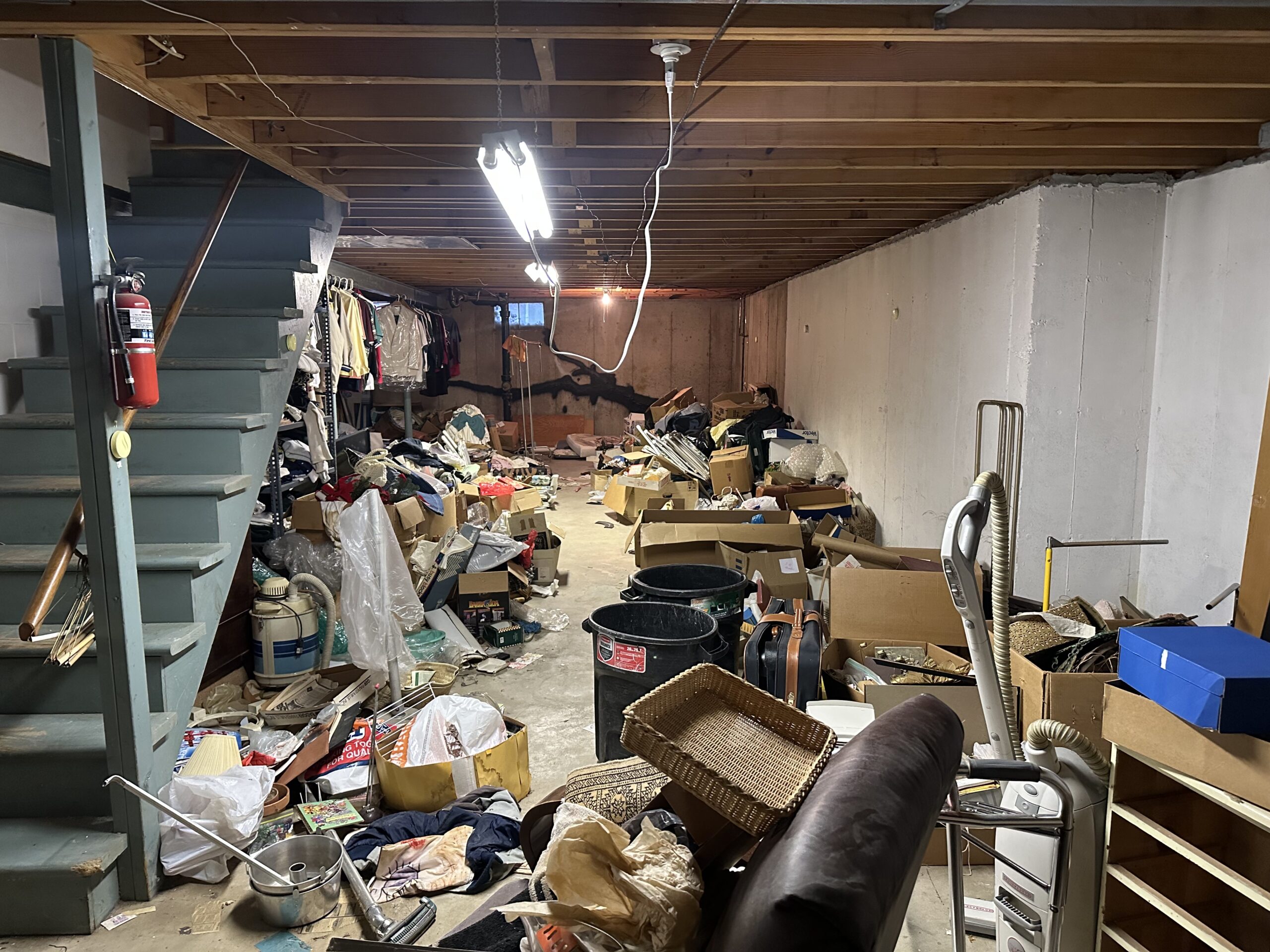 Cluttered basement before cleanout, filled with boxes, old furniture, household junk, and debris, highlighting the need for basement junk removal services.